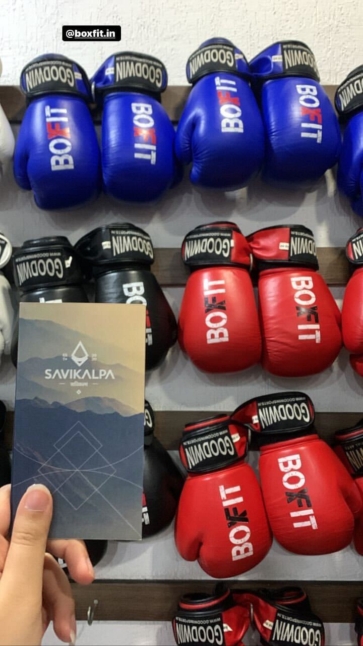 Display of various boxing gloves on a wall rack at BoxFit gym, with a Savikalpa promotional brochure held in front of them
