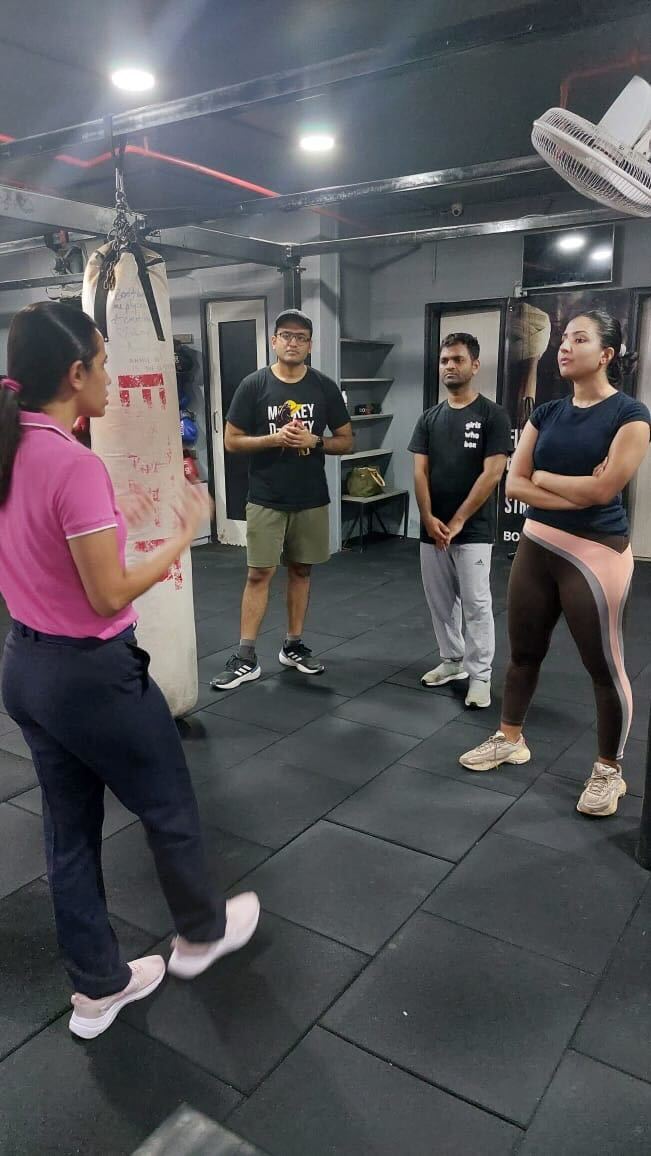 Group of people engaging in a discussion inside a gym, surrounded by fitness equipment like punching bags and exercise mats