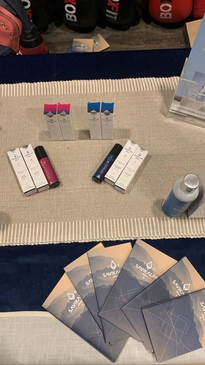 Table display of Savikalpa products including pain relief oils and roll ons, arranged with promotional brochures at an event