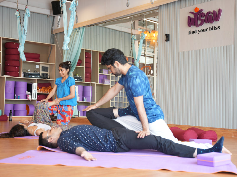 Instructors assisting participants with massage techniques in a yoga studio with mats at a bodywork workshop by Savikalpa