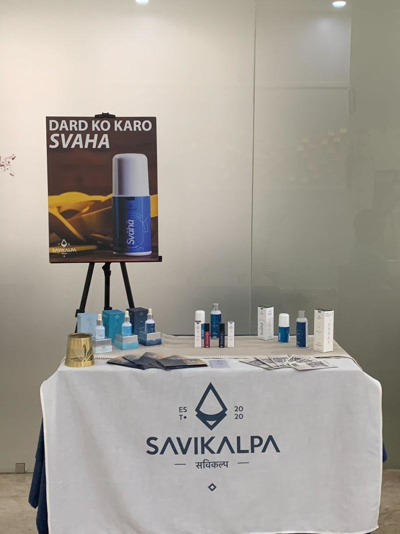 Products display on a table covered with a Savikalpa branded cloth at a workshop, featuring oils, cream & roll ons.