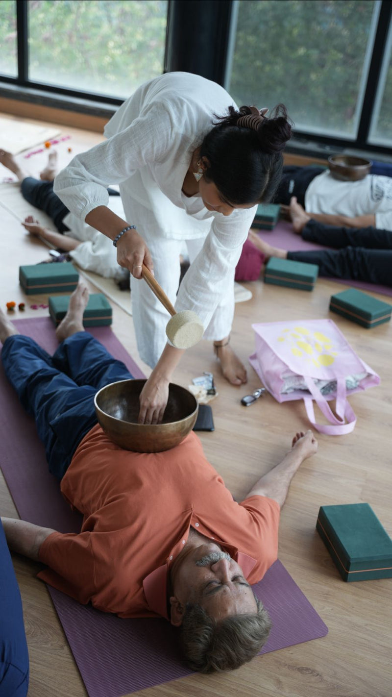 Yoga instructor using a singing bowl on a participant's chest in a yoga studio, enhancing the relaxation experience