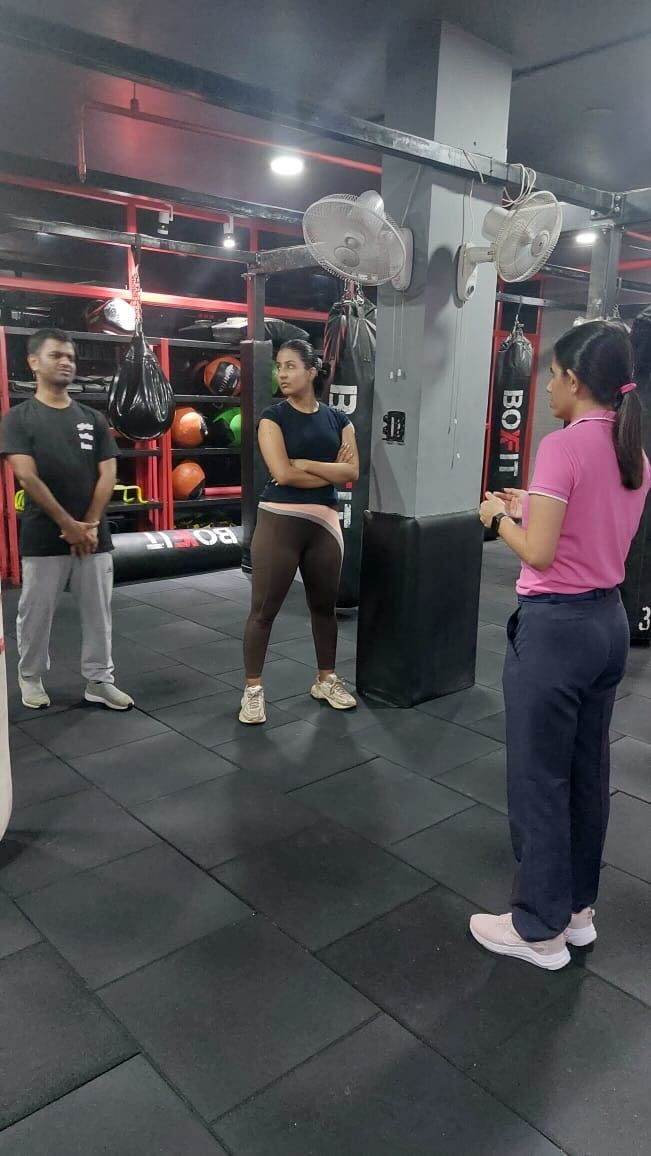 Three individuals in a conversation, standing near boxing and fitness training equipment at Savikalpa event